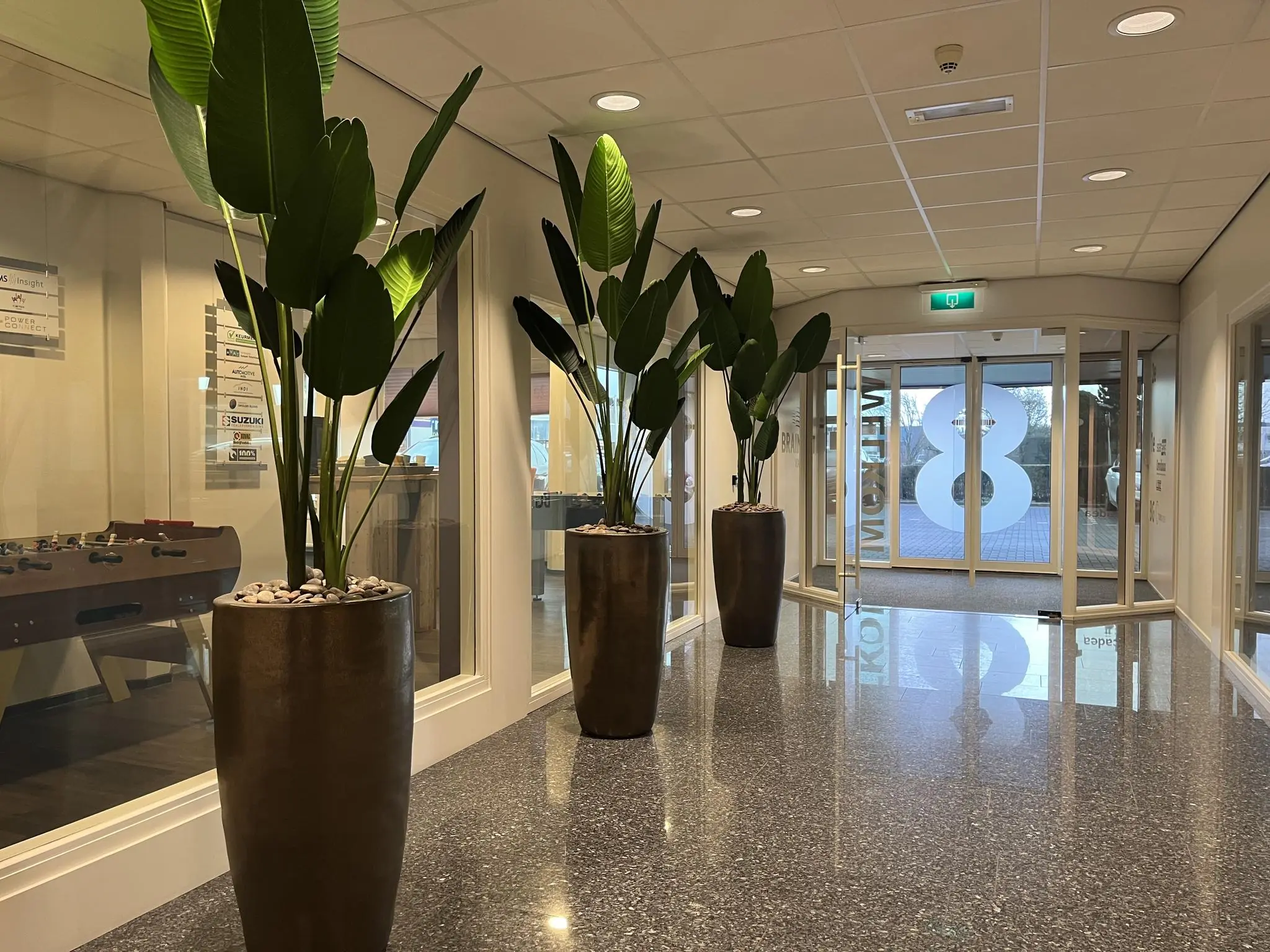 Verlichte kantoorhal aan de Lange Dreef met grote plantenbakken en glazen draaideur met het cijfer 8.